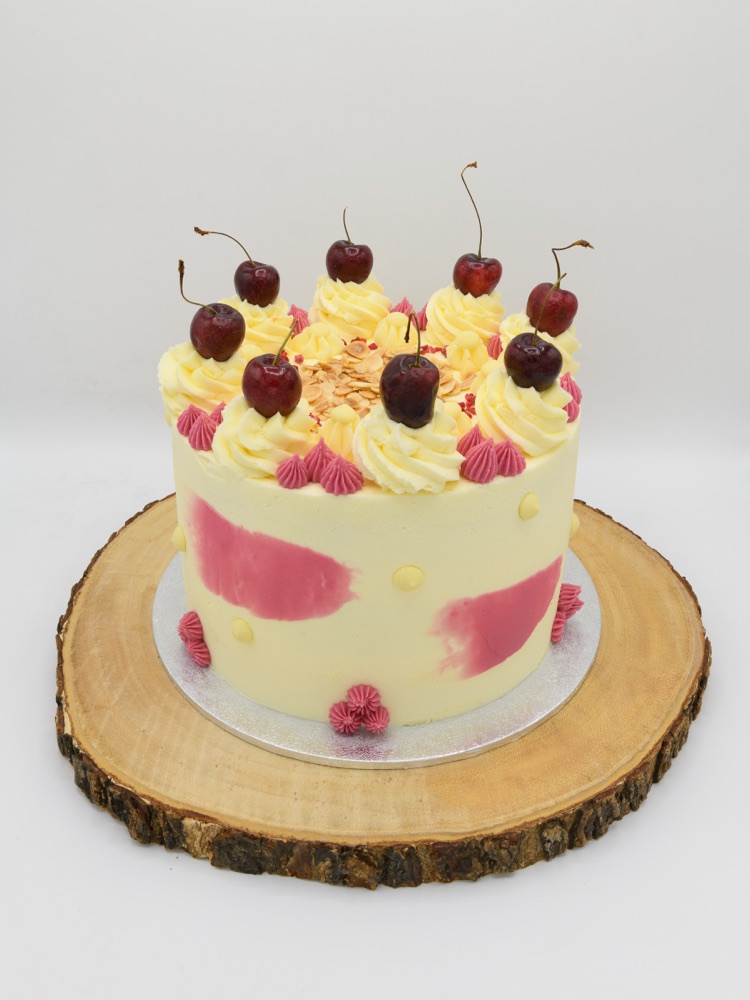 A handcrafted celebration cake by Bakes By Holly, decorated with fresh cherries and buttercream